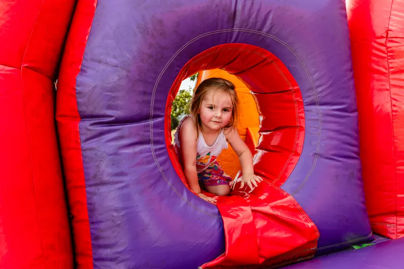 A smiling toddler peeks out through a round opening in a red and purple inflatable.