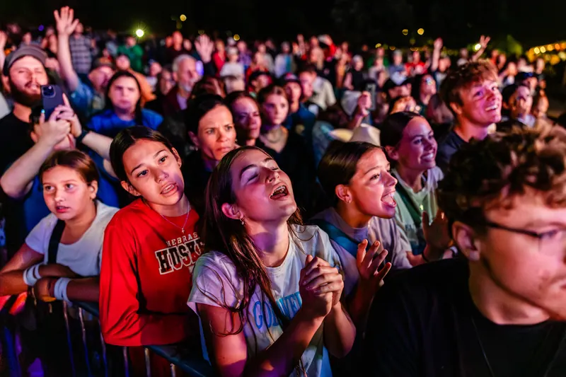 Teenagers and families pack together near the stage at night, watching the show with excited faces.