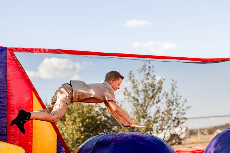 A boy dives headfirst across an inflatable obstacle course on a sunny afternoon.