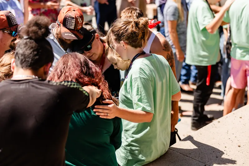 A small group gathers close with hands on shoulders to pray together in the amphitheater.