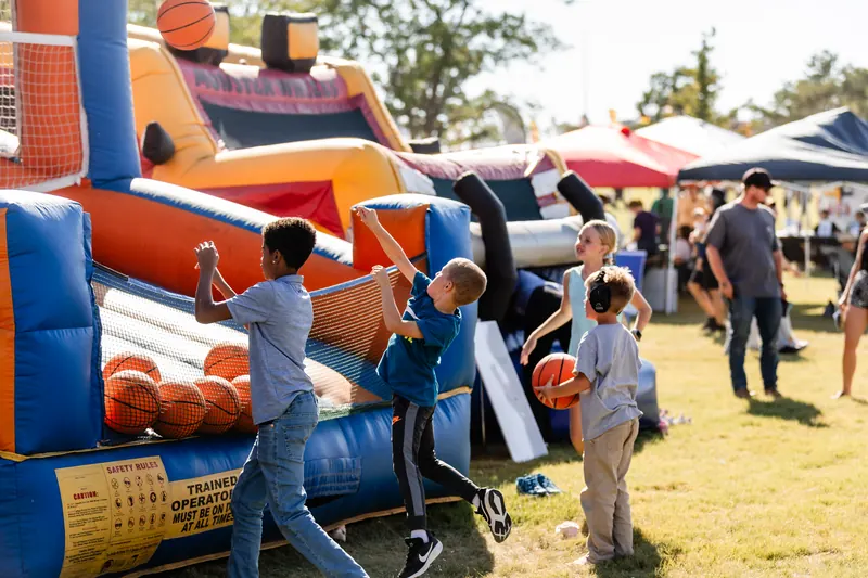Kids shoot basketballs at an inflatable hoop game on a sunny afternoon.