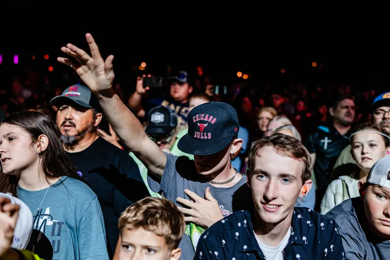 A young man grins in the middle of a night crowd as people around him cheer and raise their hands.