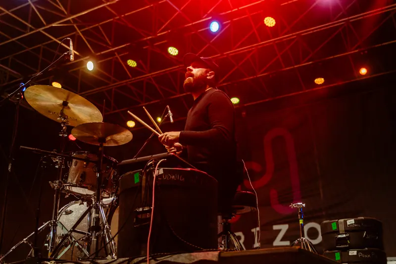 A drummer plays under red stage lights with the Horizon logo on the backdrop.