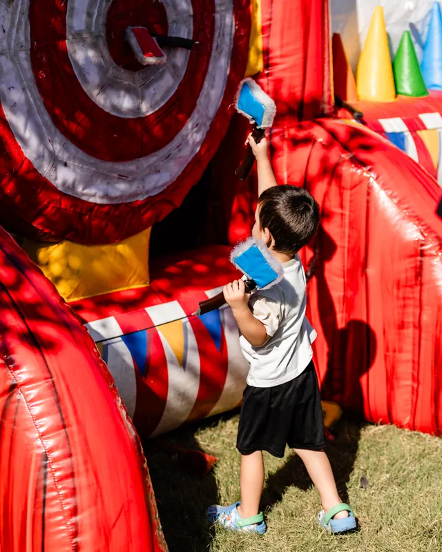 A young child stands in front of a giant inflatable dart board holding a ball.