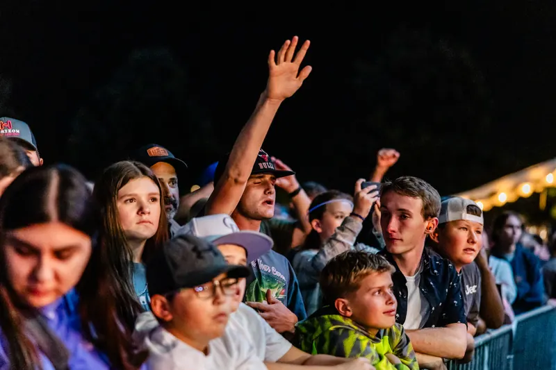 Kids and teens near the front of the stage at night, one with an arm raised high.