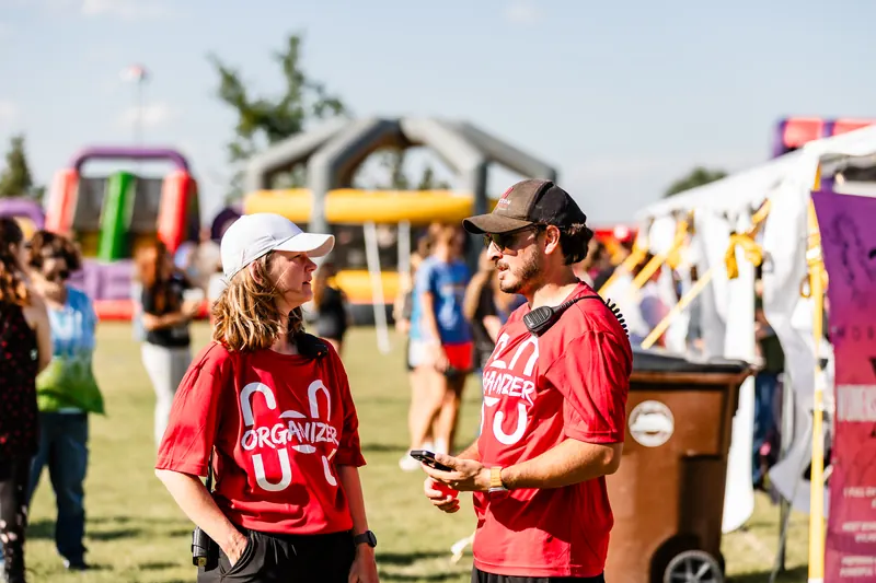 Two festival organizers in red shirts talk on the grounds near the inflatables.